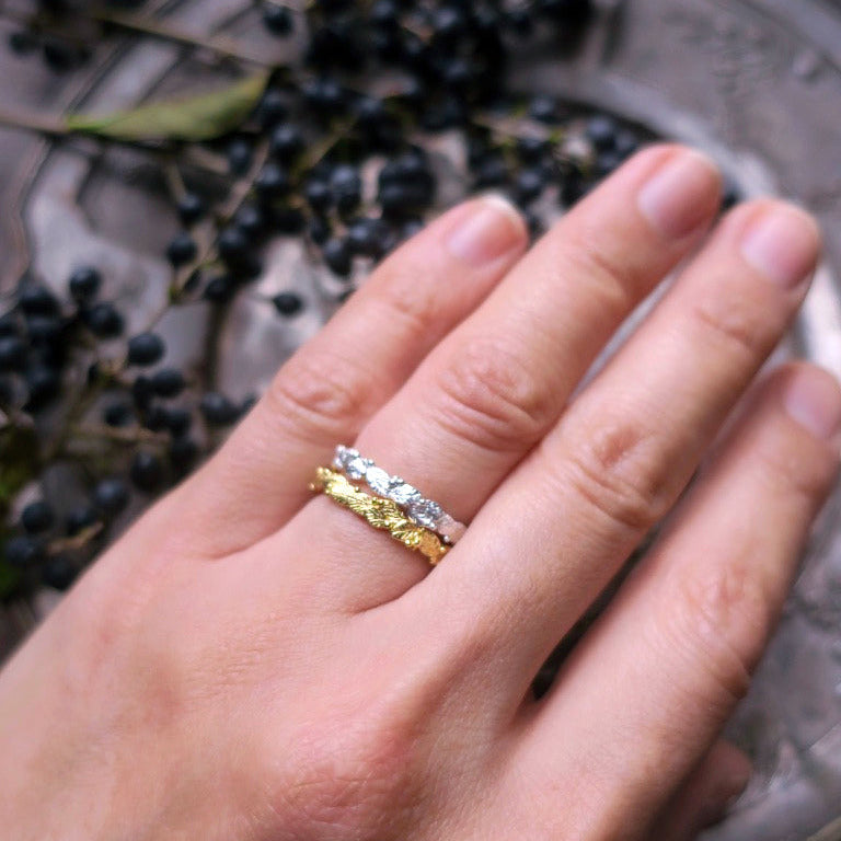 Stacked botanical rings in gold-plated silver and sterling silver worn together, showing detailed leaf and morning-dew motifs — nature-inspired handcrafted jewelry with refined textures.
