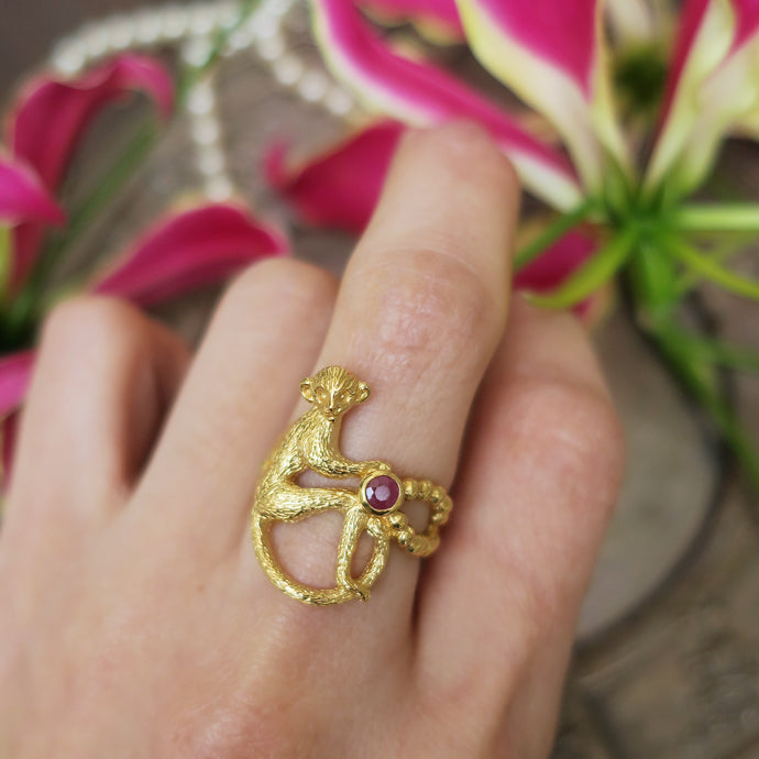 Handcrafted 18K gold-plated monkey ring with an opaque ruby, worn on a finger — a sculptural piece that evokes a mischievous scene from a French salon.