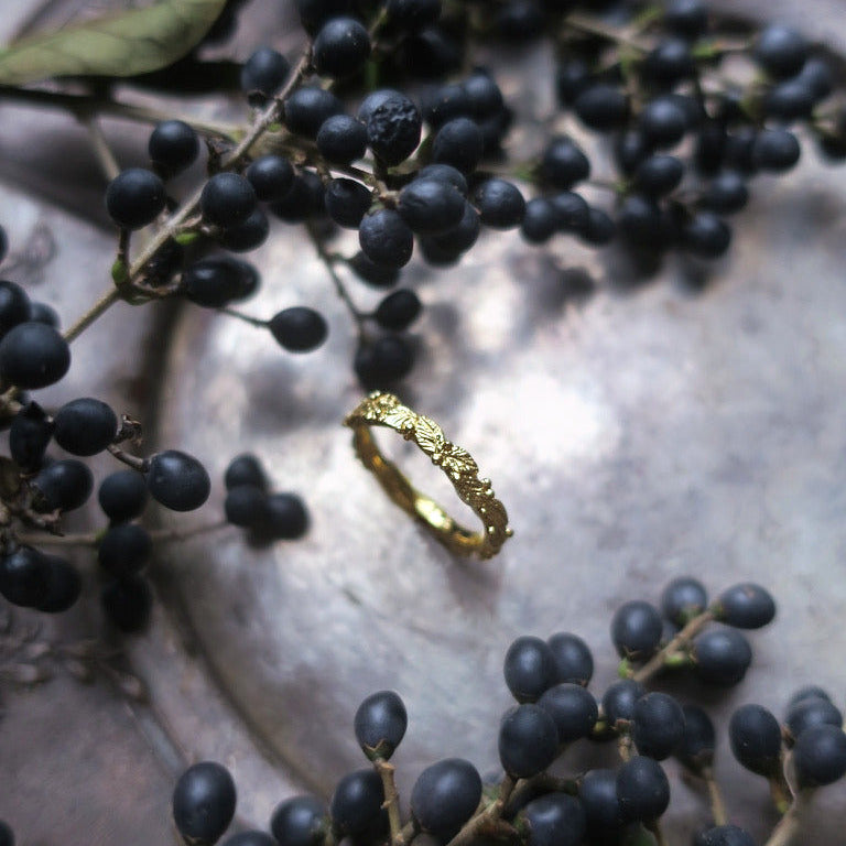 Nature-inspired botanical ring resting on dark berries and foliage, showing detailed leaf motifs and morning-dew textures — hand-sculpted gold-plated silver jewelry.