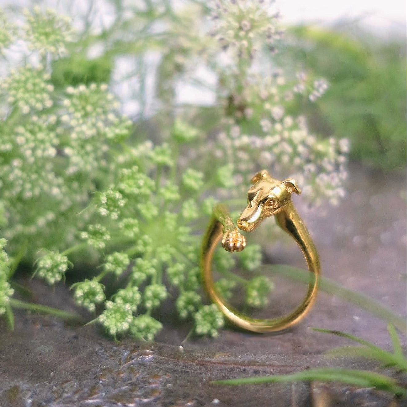 Gold Sighthound dog ring resting among green flowers — the “Guardien” piece inspired by Italian Greyhounds and Whippets, hand-sculpted in Paris in sterling silver with 18K gold plating.