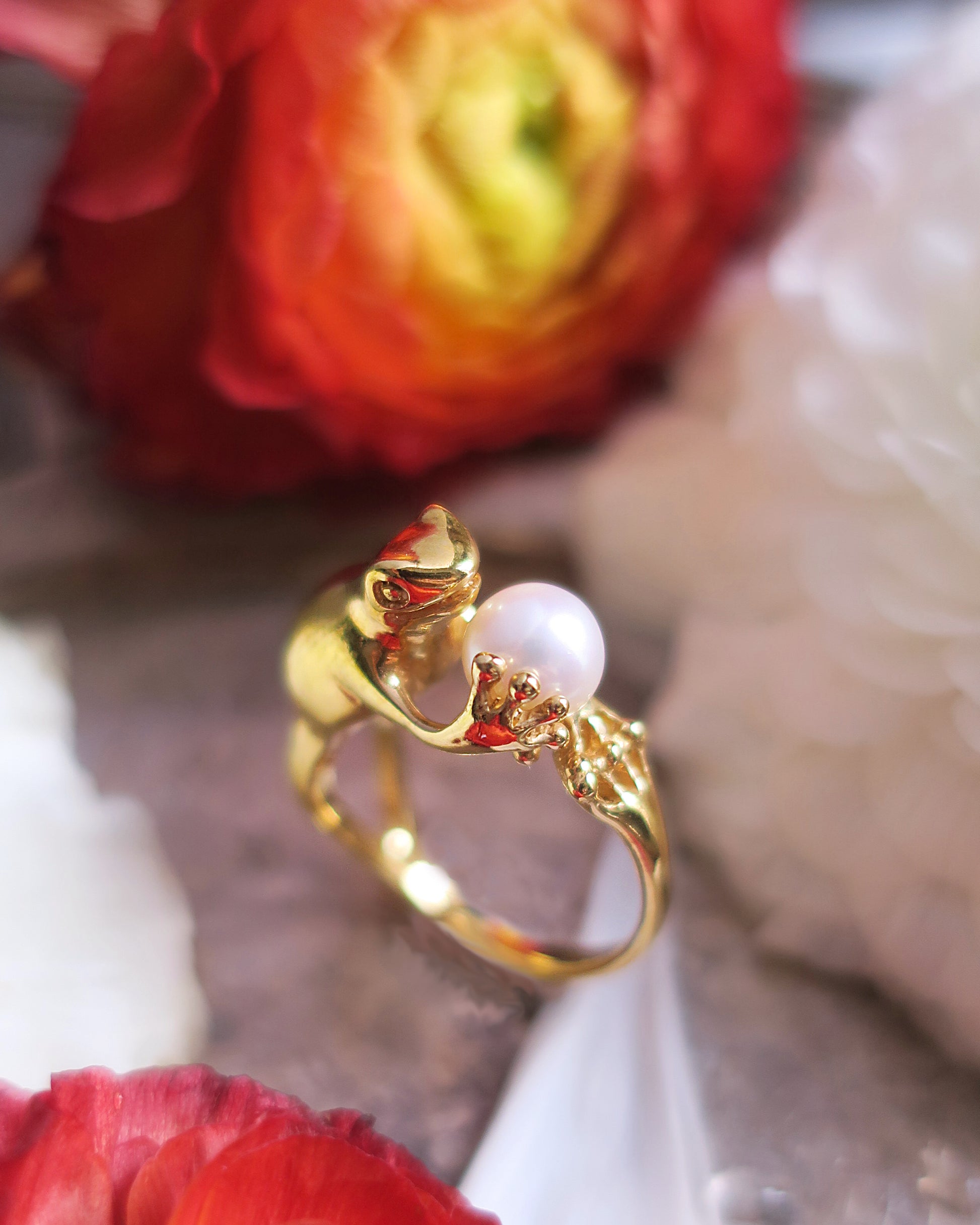 Gold-plated silver frog ring with a freshwater pearl photographed with red and white flowers, poetic Art Nouveau animal jewelry.
