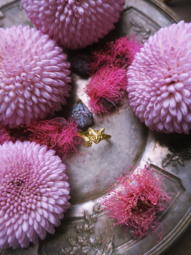 Cat face and paw ring in gold, styled among pink florals to highlight its whimsical design and refined hand-carved details. Paris-crafted animal jewelry featuring a discreet paw pad motif.