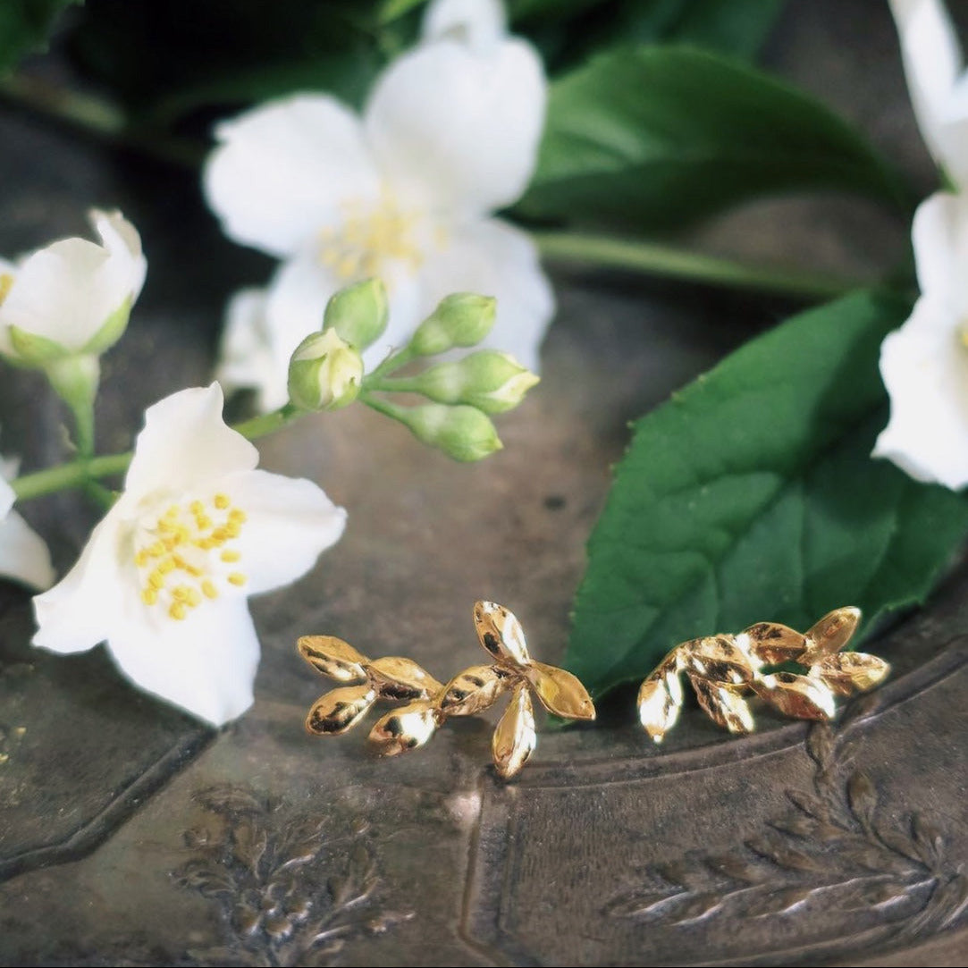Asymmetrical laurel leaf earrings in 18K gold-plated silver, hand-sculpted in Paris and styled with green leaves and flowers for botanical mood.