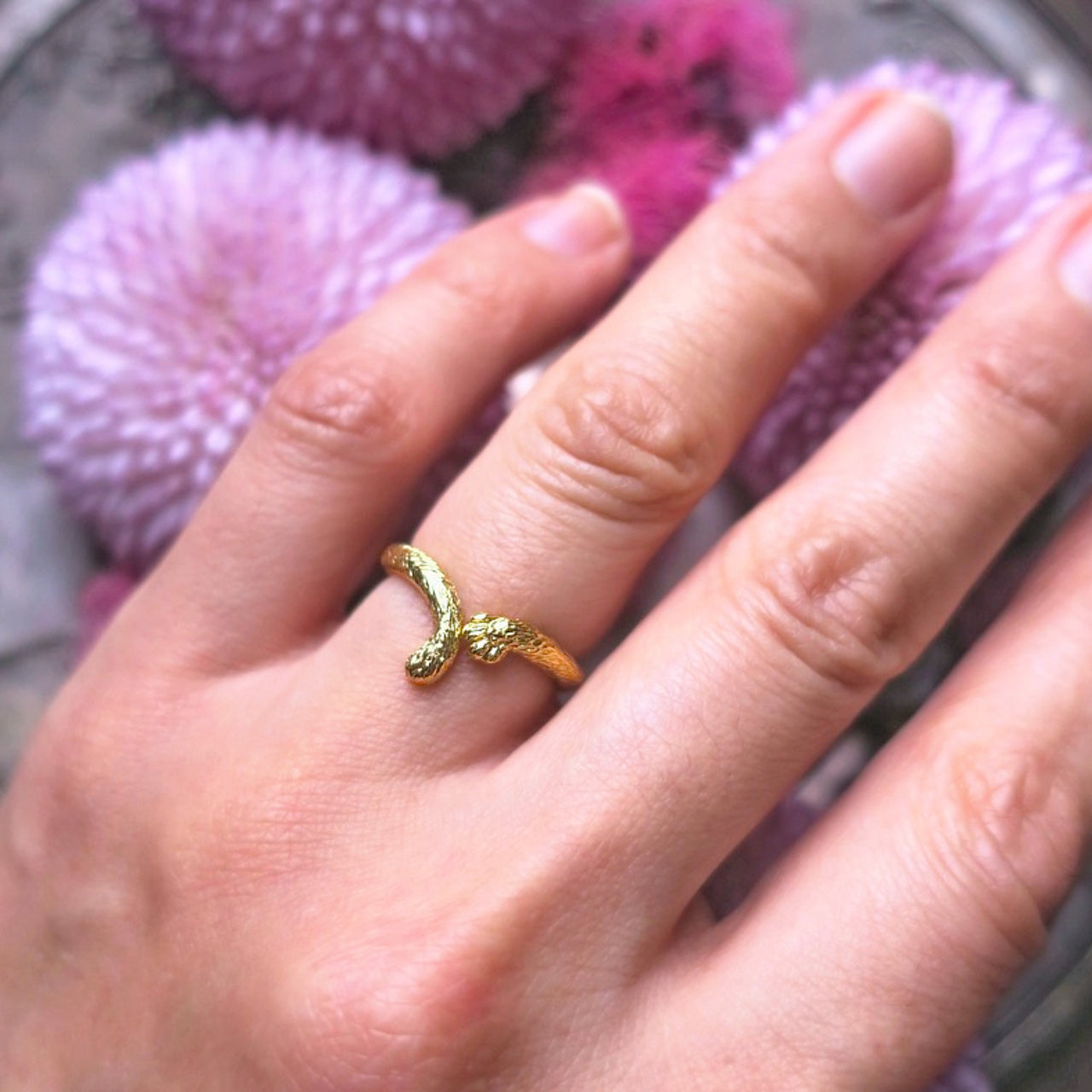 Cat tail and paw ring in 18K gold-plated silver 925 held in hand, showing sculptural form among purple chrysanthemums