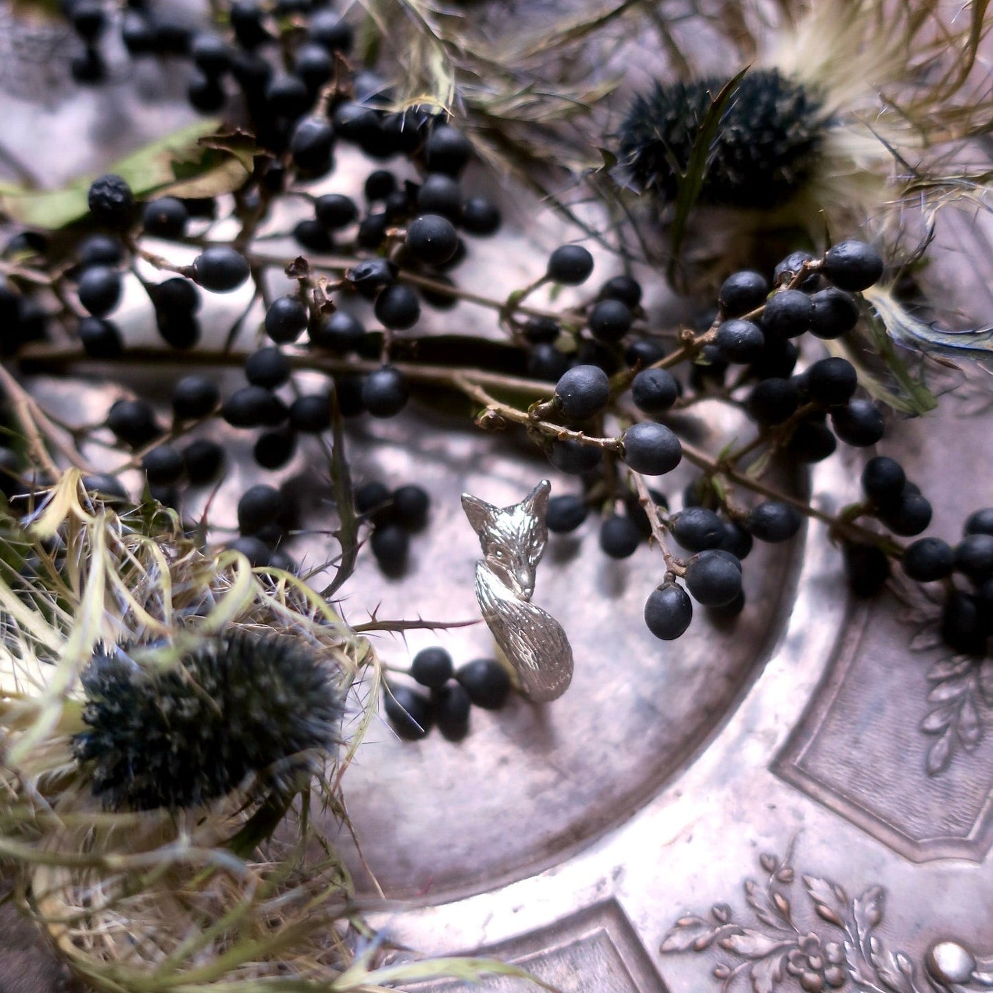 Sterling silver fox pinky ring displayed on a vintage tray with botanical elements, emphasizing its fine texture, hand-crafted detail and elegant animal-themed design.