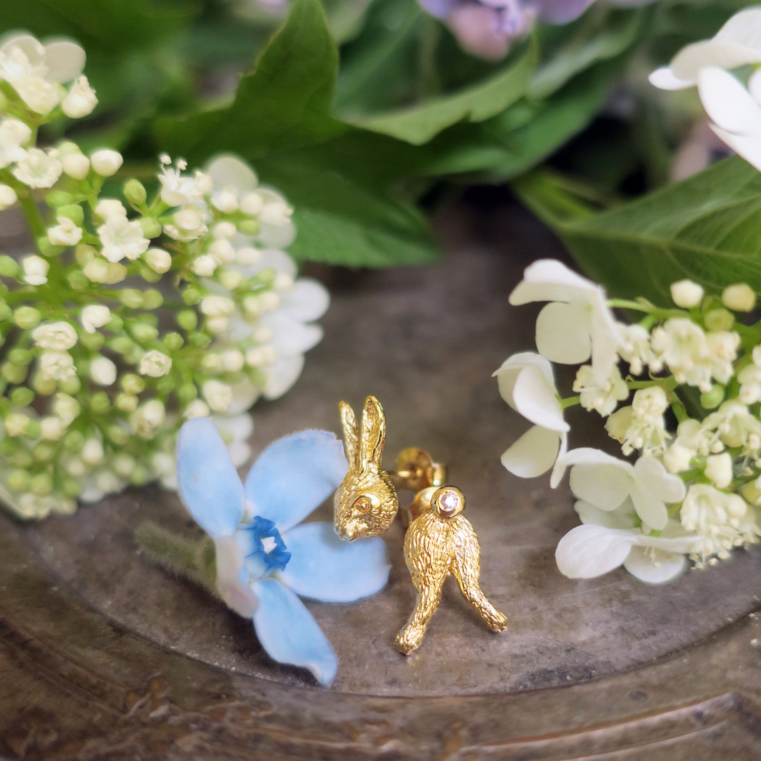 Sculpted gold rabbit earrings in gold-plated sterling silver displayed with flowers, playful yet refined animal jewelry with a white sapphire detail.