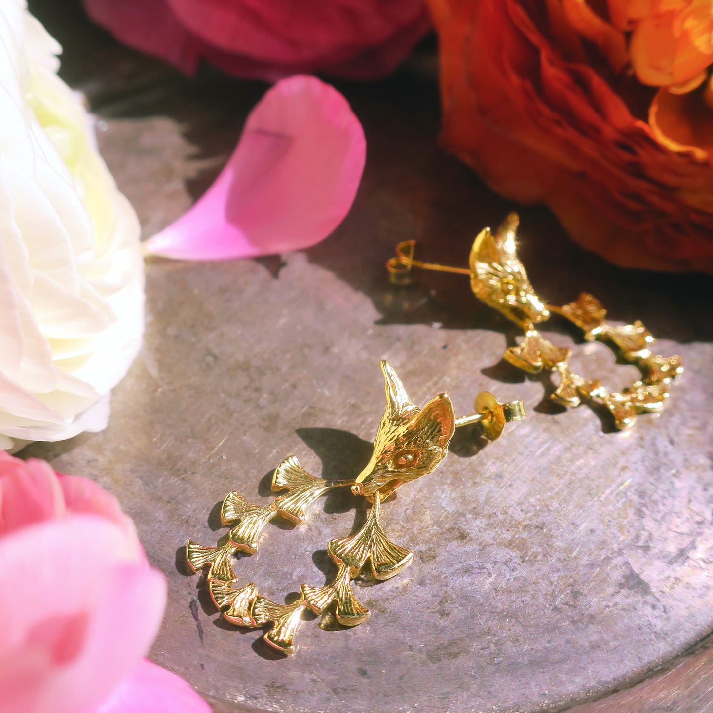 Gold fox & ginkgo leaf earrings styled with floral studio setting – nature inspired artisan jewellery Paris.