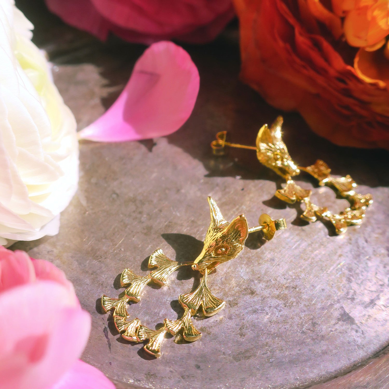 Gold fox & ginkgo leaf earrings styled with floral studio setting – nature inspired artisan jewellery Paris.
