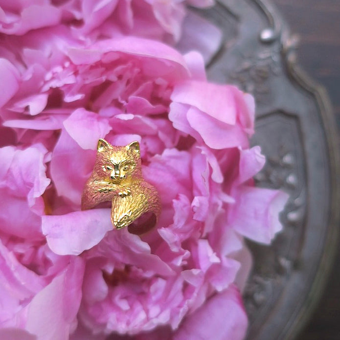 Small gold-plated silver cat ring displayed on a vintage tray with flowers, highlighting its voluminous long-hair texture. Handcrafted animal jewelry made in Paris.