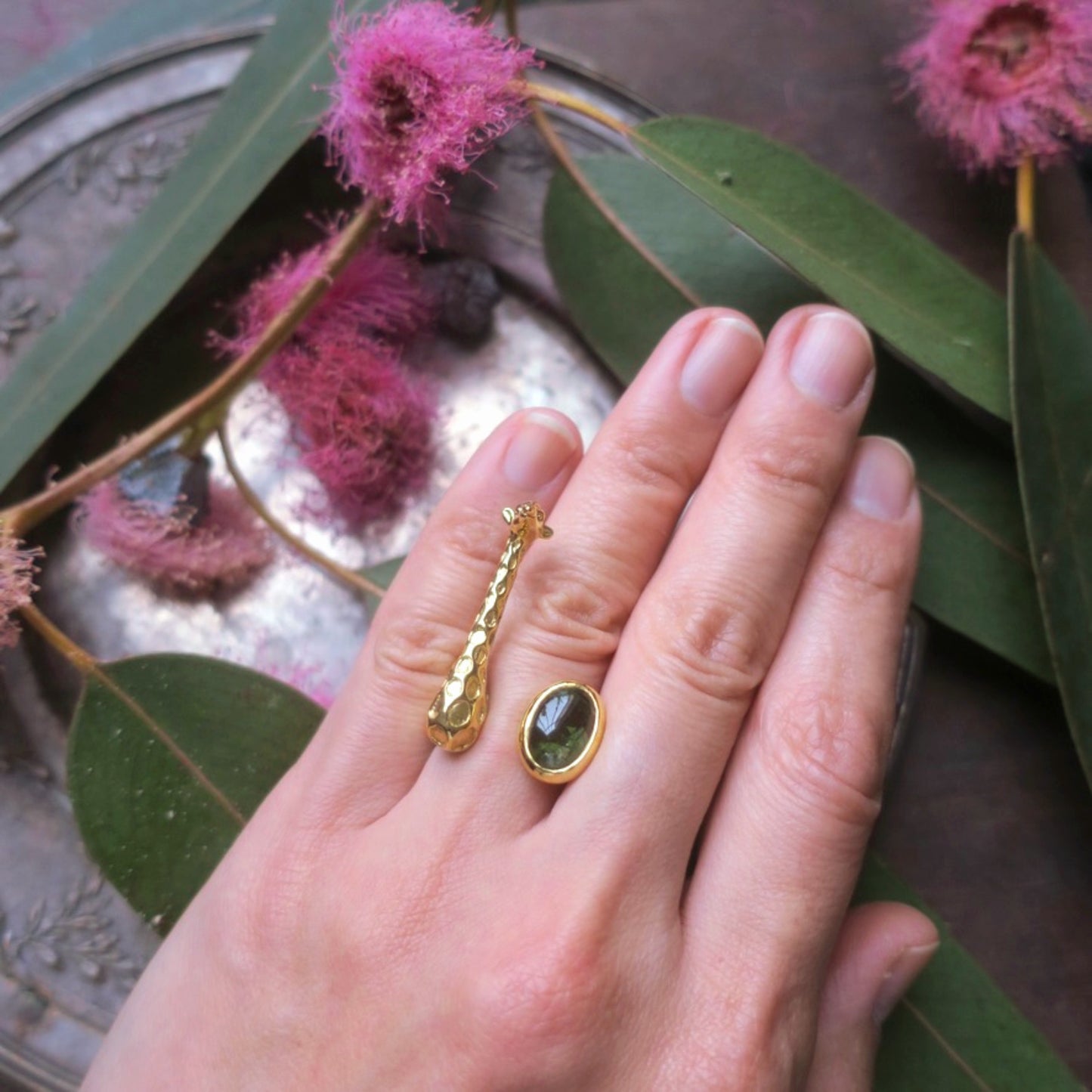Gold giraffe ring with green tourmaline worn on the hand, showing the sculptural animal design and natural gemstone details.
