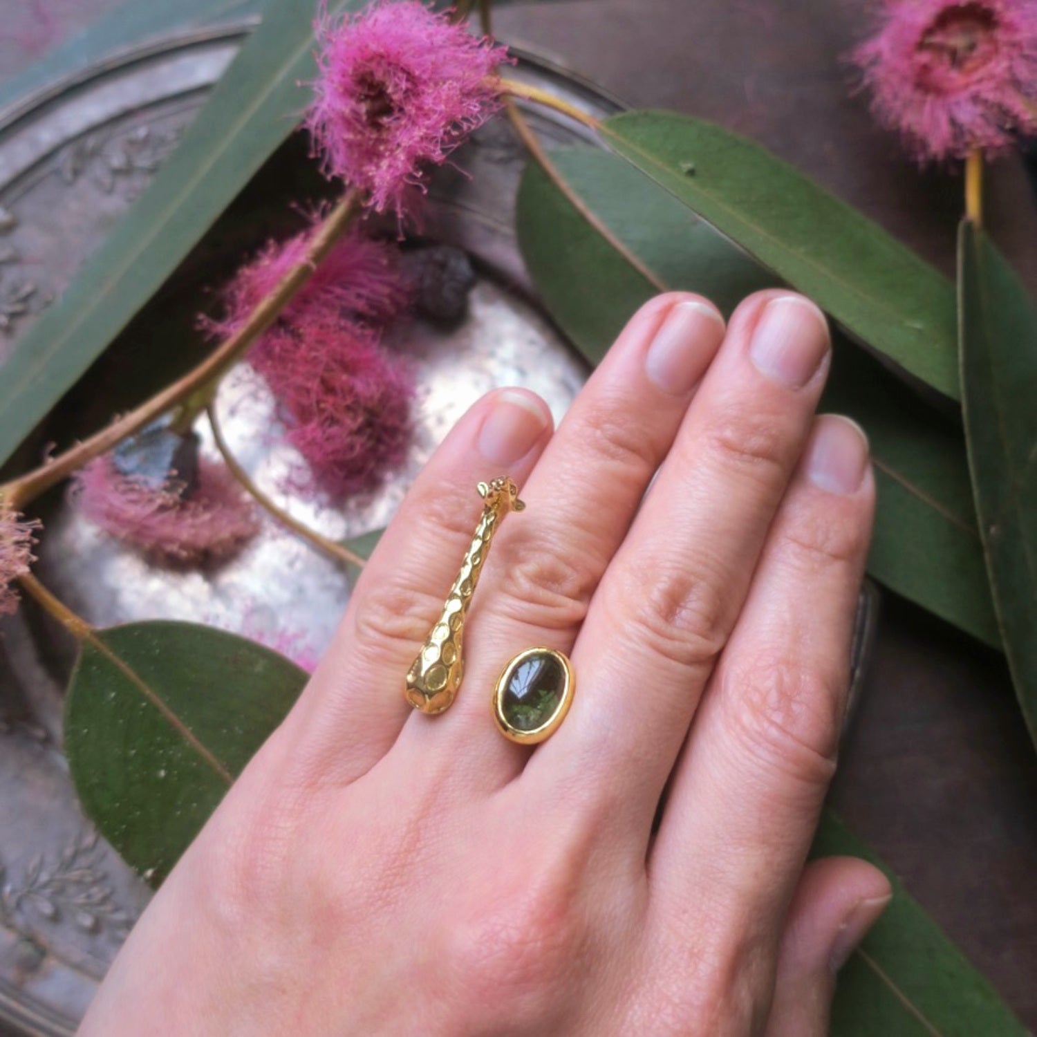 Gold giraffe ring with green tourmaline worn on the hand, showing the sculptural animal design and natural gemstone details.