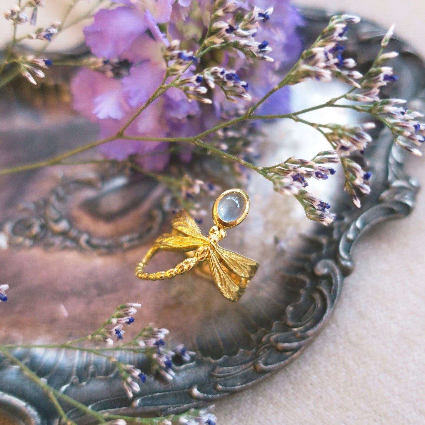 Milky aquamarine dragonfly ring placed on vintage silver tray with lilac flowers, evoking Art Nouveau romanticism and poetic craftsmanship.
