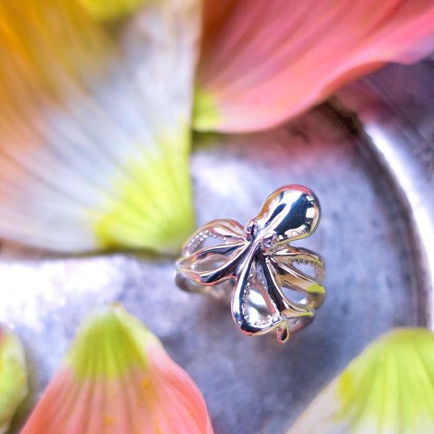 Solid silver octopus ring photographed with soft floral background, highlighting the fluid tentacle silhouette; ocean-themed artisanal jewelry with bold marine-inspired design.