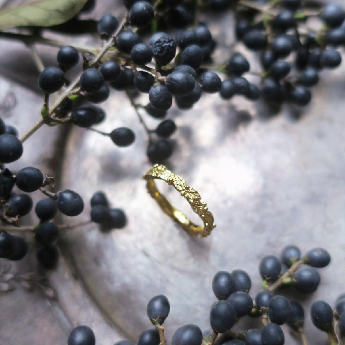 Botanical ring resting on dark berries and foliage, showing detailed leaf motifs and morning-dew textures 