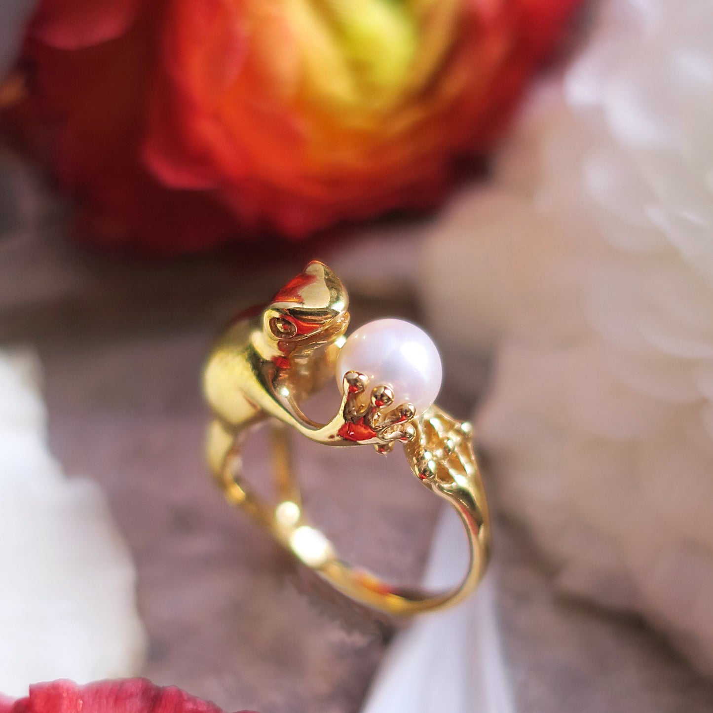 Gold-plated silver frog ring with a freshwater pearl photographed with red and white flowers, poetic Art Nouveau animal jewelry.
