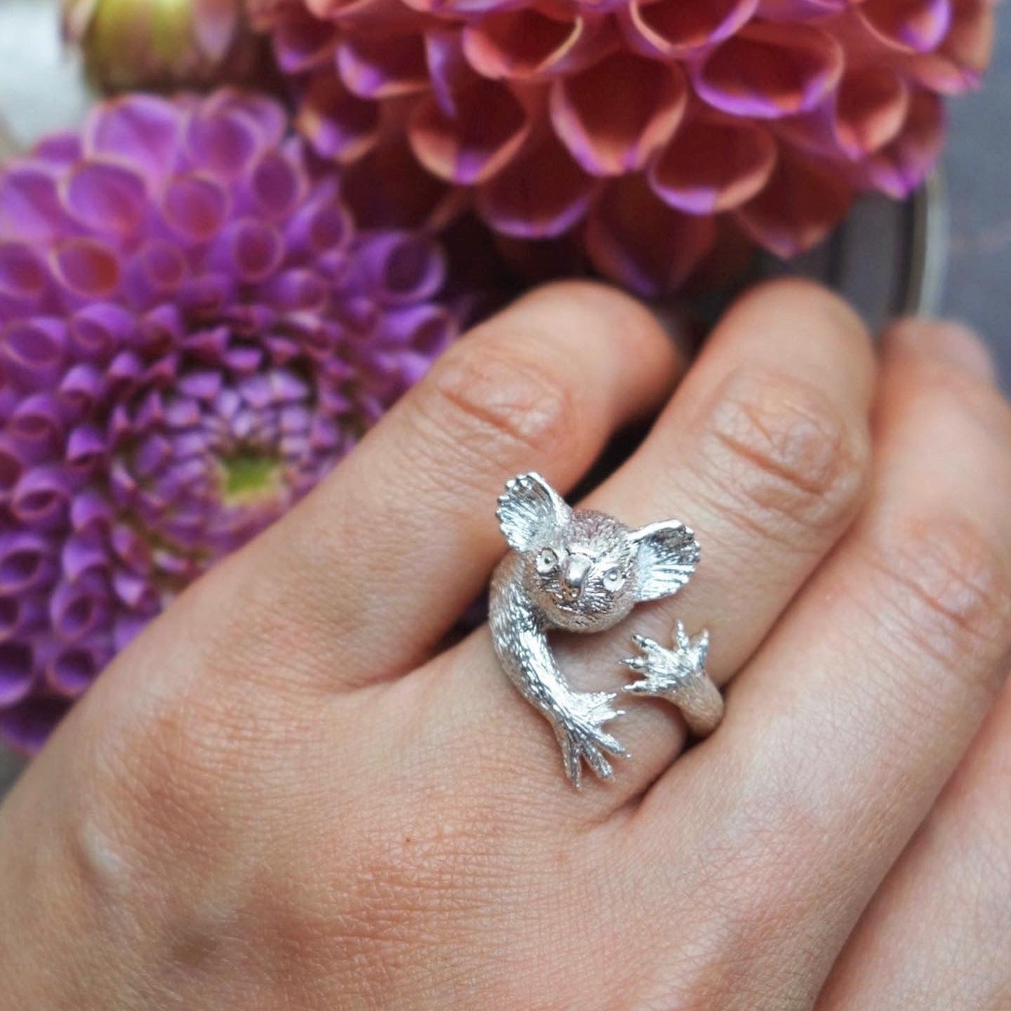 Koala ring in sterling silver worn on finger hugging pose with dahlia