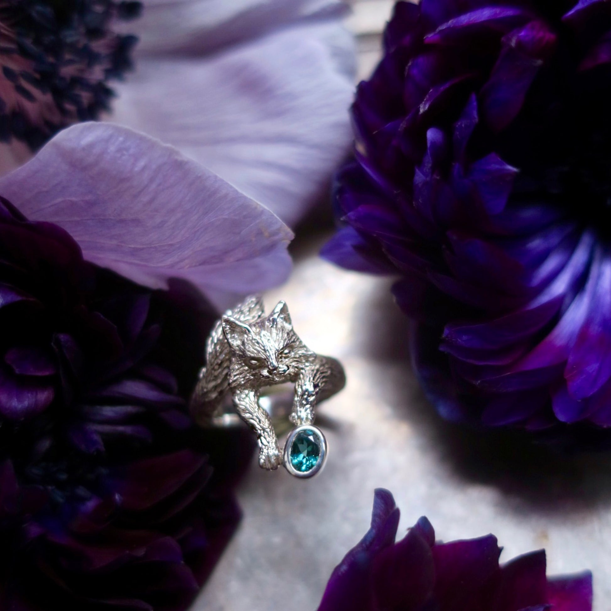 Leonardo Maine Coon cat ring in sterling silver photographed among deep purple anemones, featuring a natural blue-green tourmaline