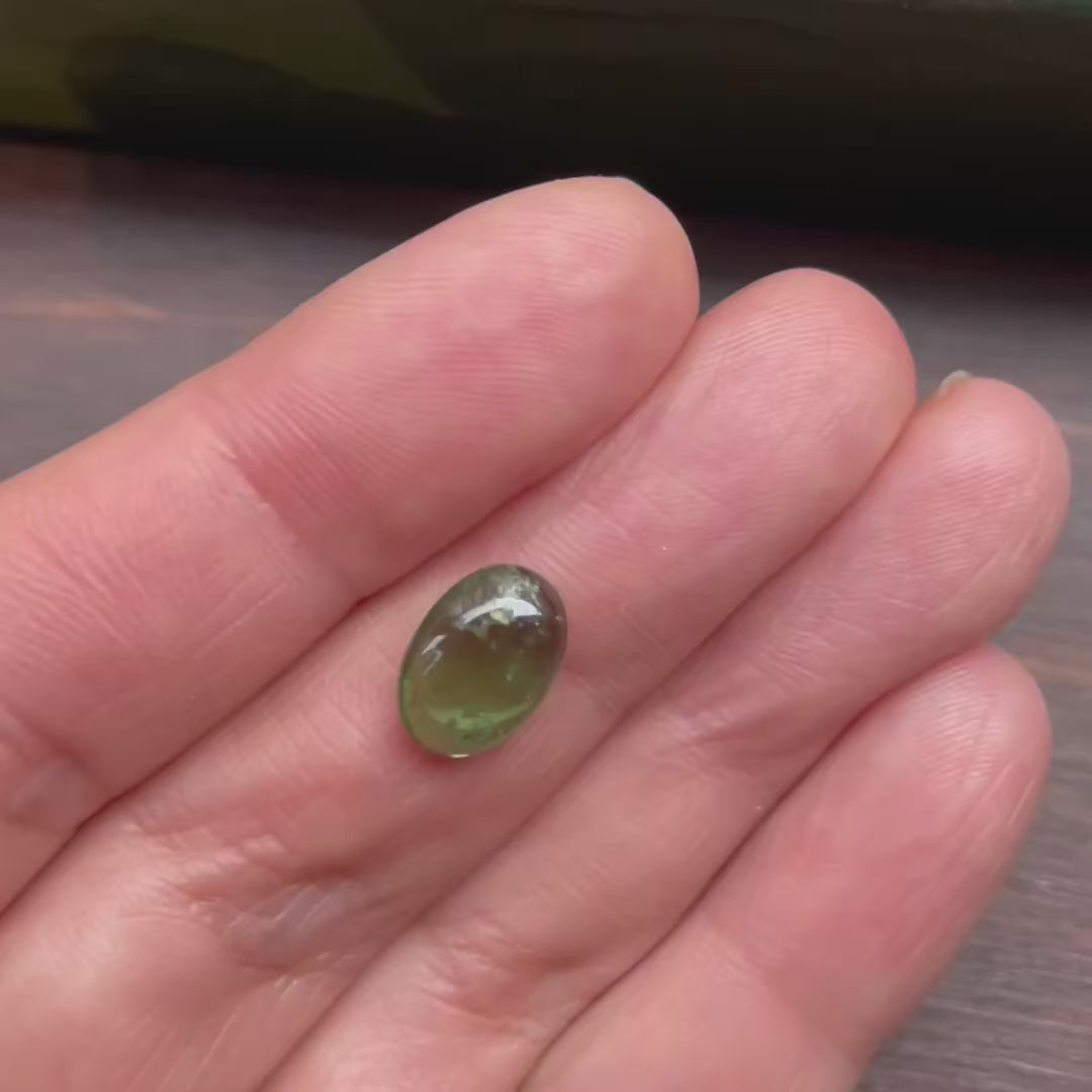 Natural green tourmaline loose gemstone on hand, showing inclusions and color variations in motion  