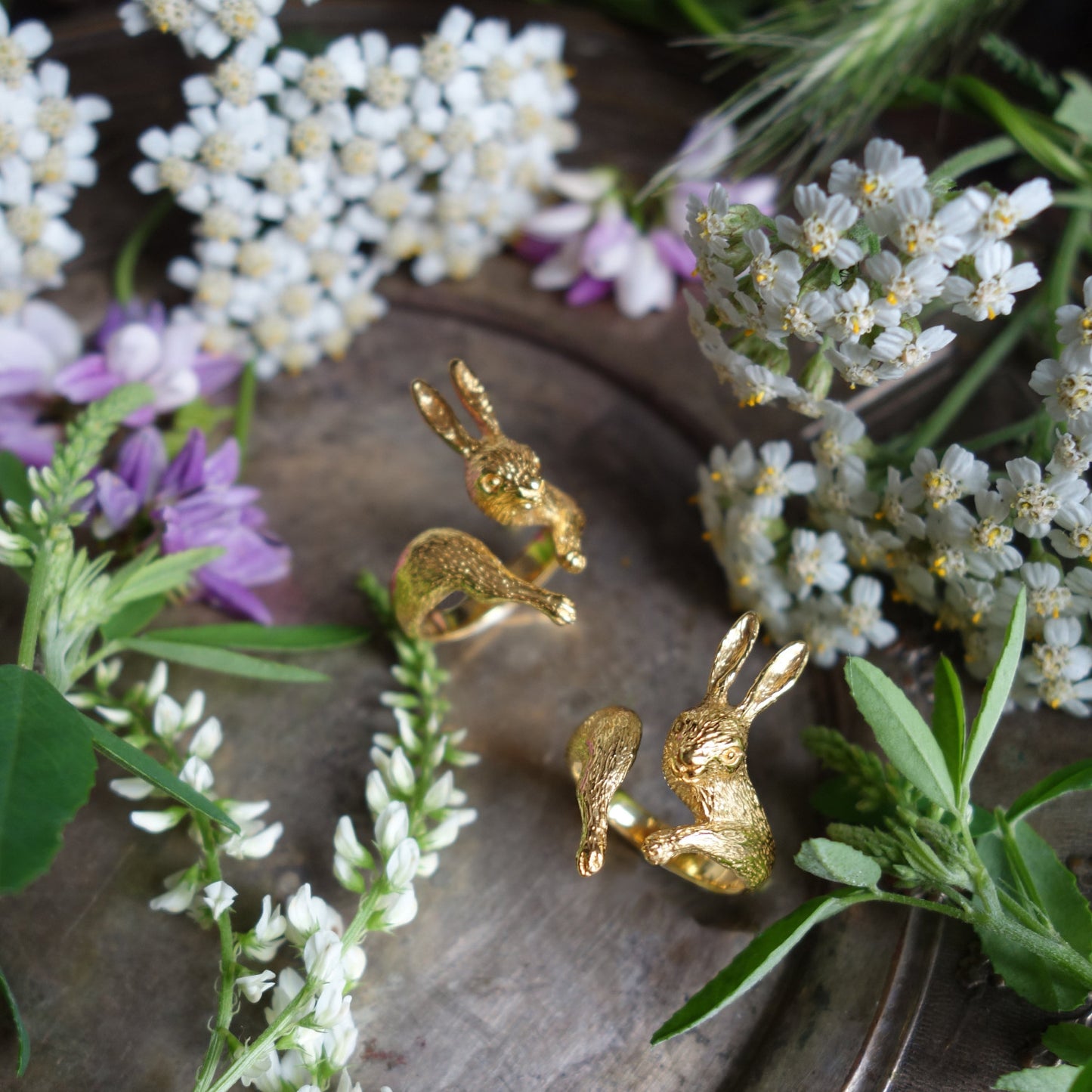 Gold rabbit rings in silver 925 arranged among wildflowers, sculpted animal jewelry