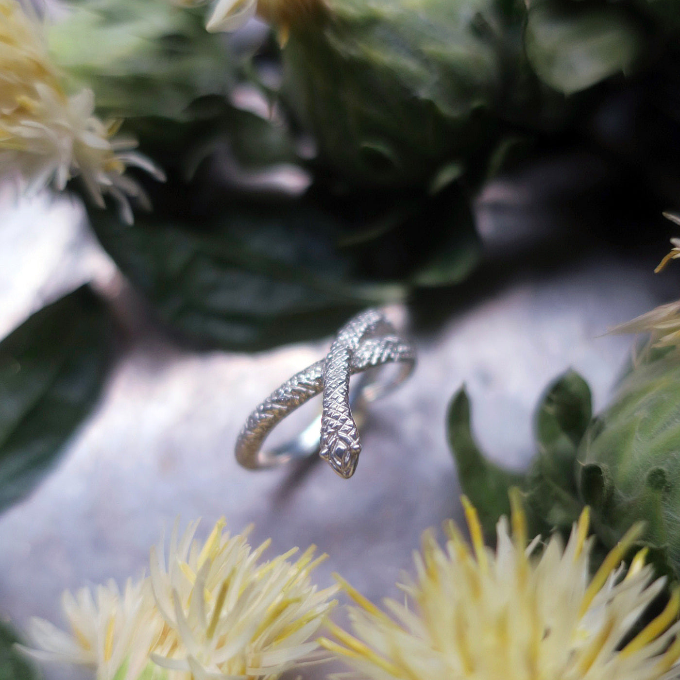 Sterling silver snake ring with detailed scales, coiled shape photographed among flowers