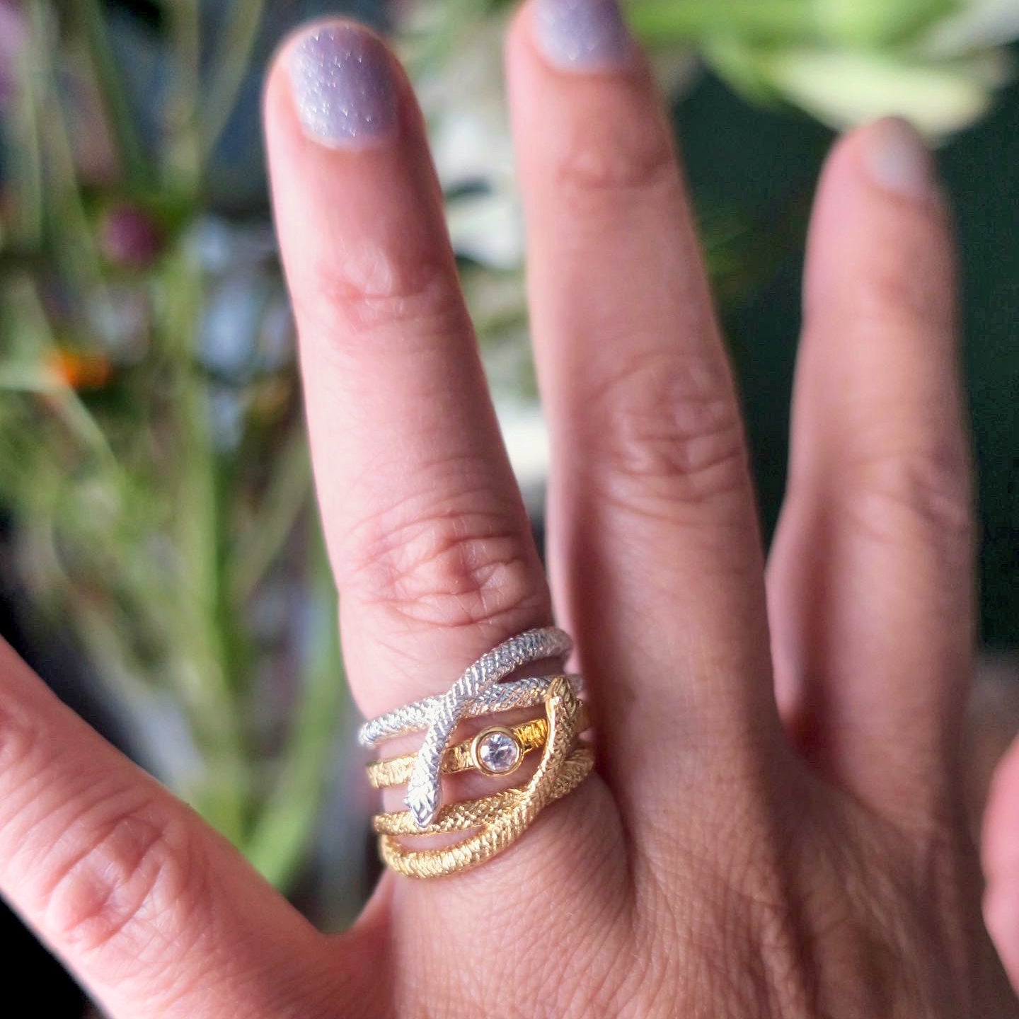 Close-up of mixed-metal snake wrap ring in sterling silver and gold-plated silver worn stacked with a solitaire ring