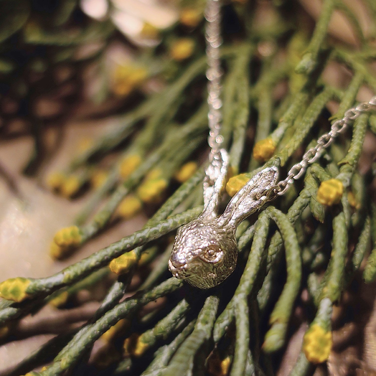 Sterling silver 925 rabbit head necklace resting on green foliage, showing the finely sculpted face and long pierced ears